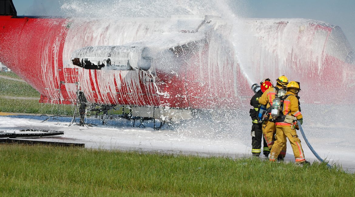 Brandweerlieden spuiten een vliegtuig met blusschuim.